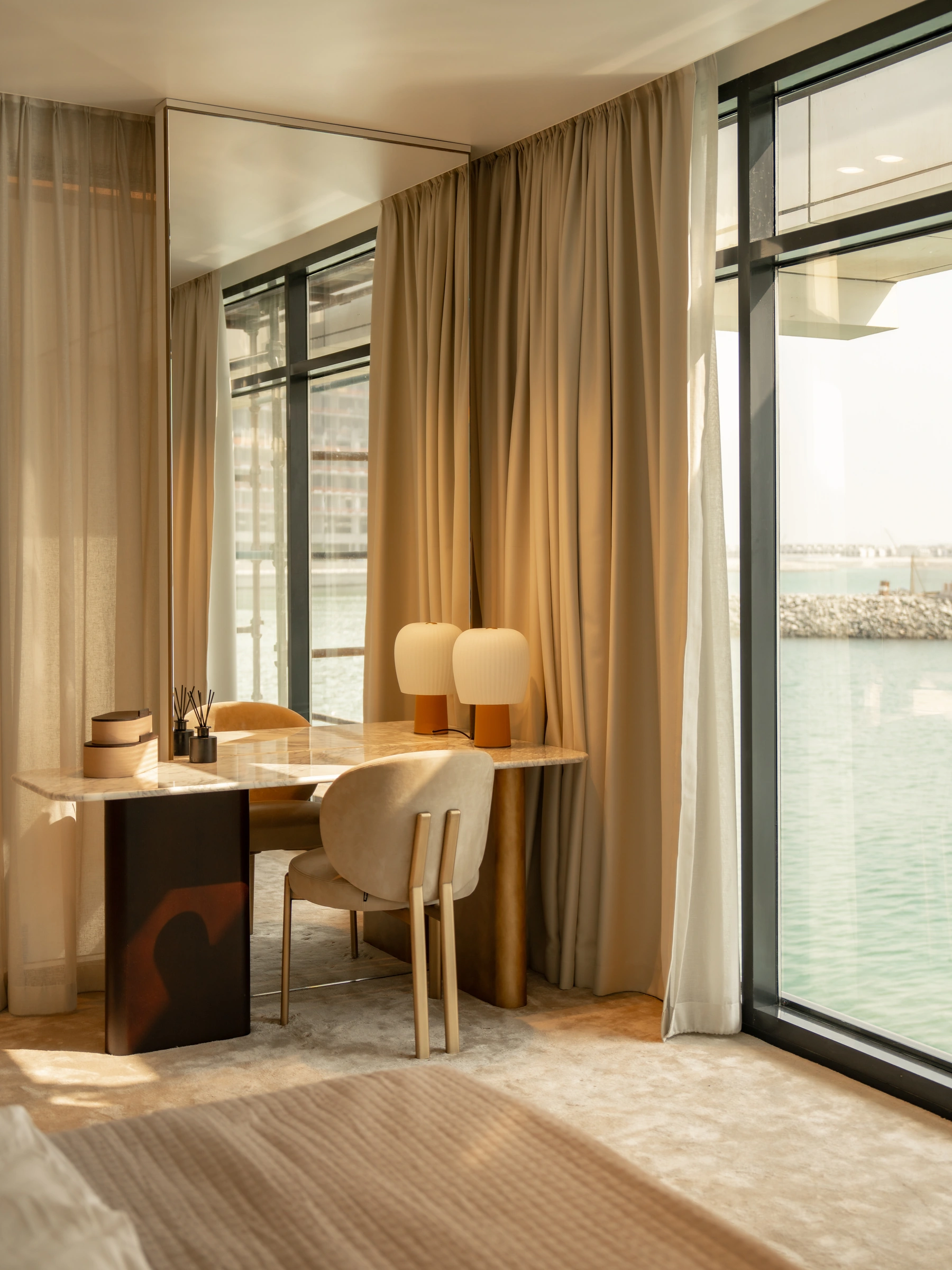 A bedroom writing desk and warm curtains beside a waterfront window