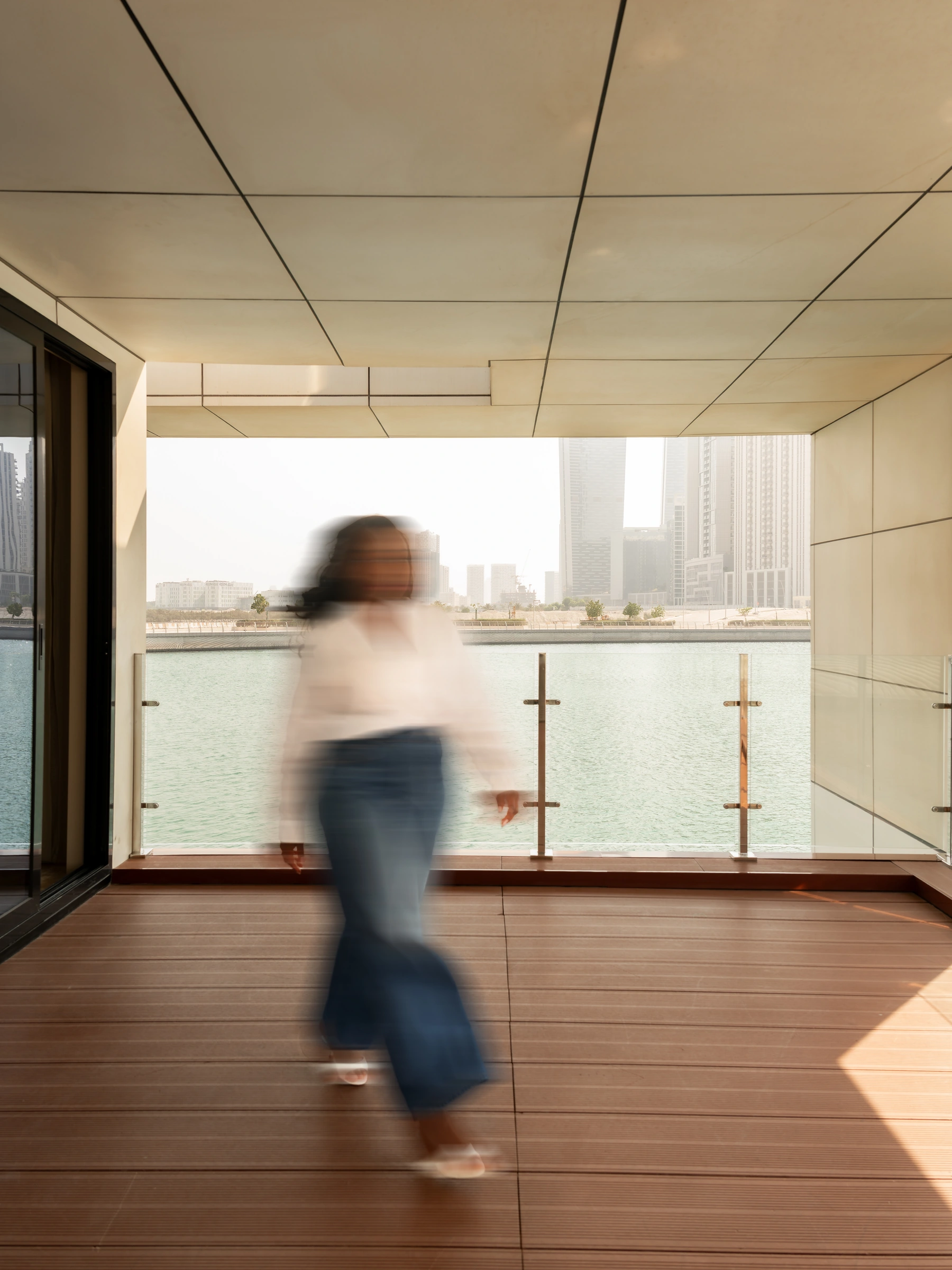 A waterfront balcony overlooking the city, with a woman walking across the terrace